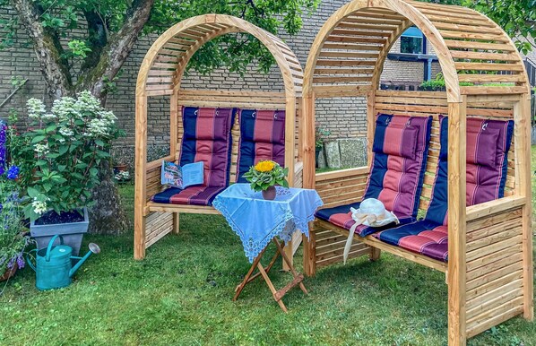 Een houten pergola met zachte zitplaatsen en een tafel met een kantoneelkleed.