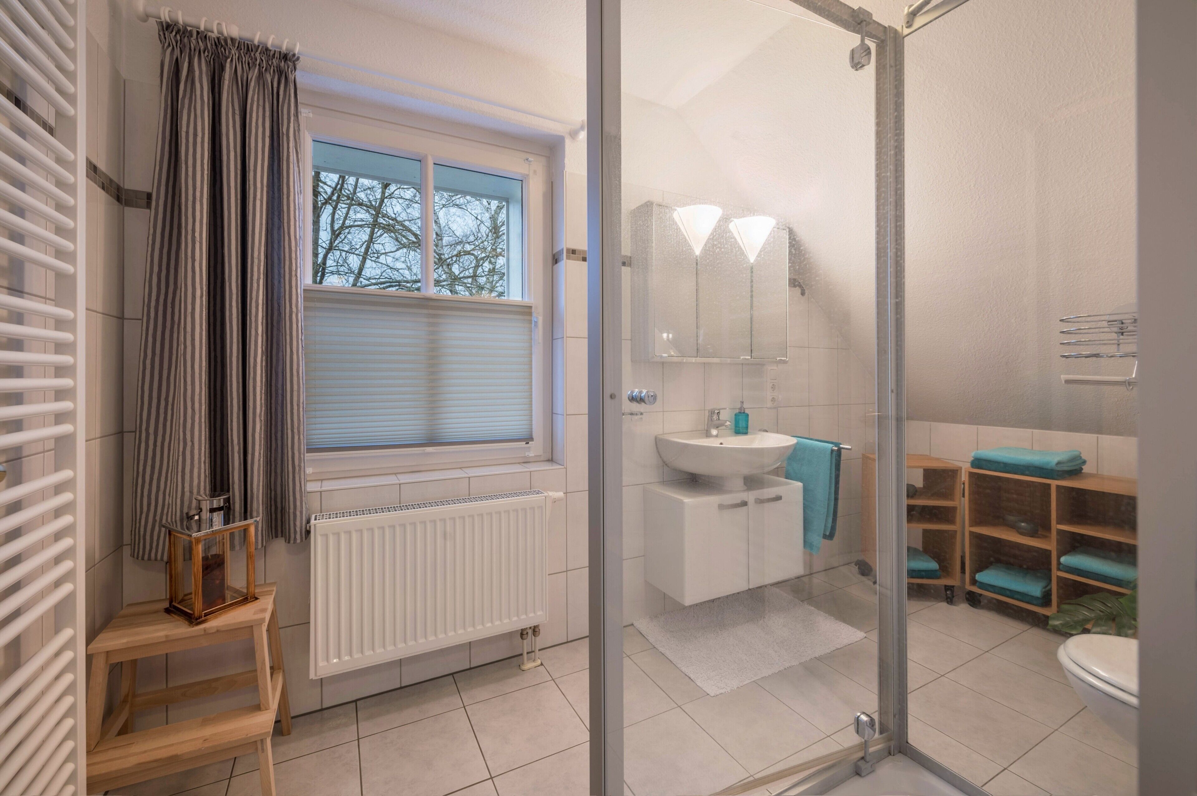 A modern bathroom with a glass shower enclosure, a white sink, and a window with curtains.