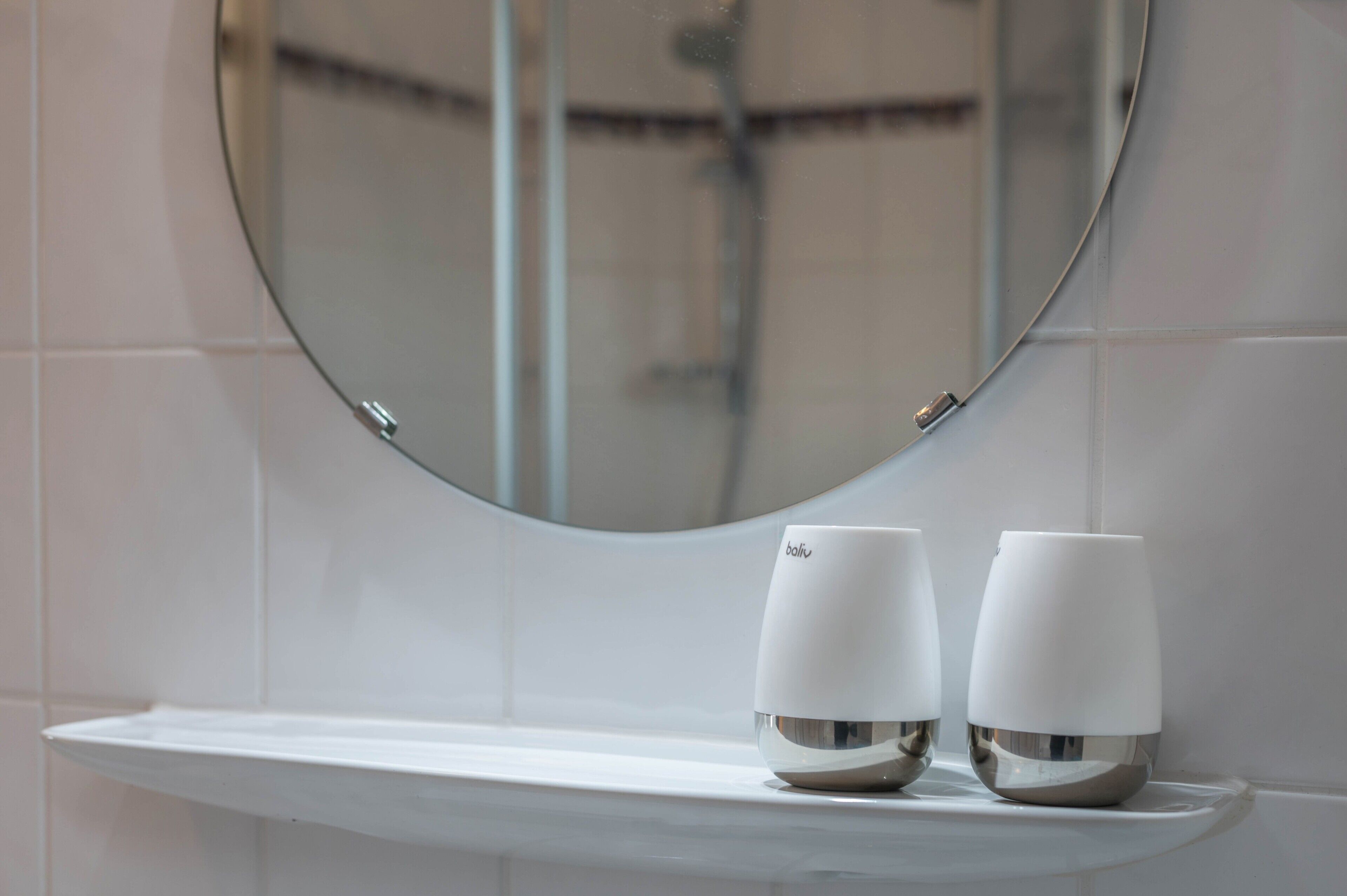 Un baño con un lavabo blanco, dos tazas blancas sobre el mostrador y un espejo redondo en la pared.