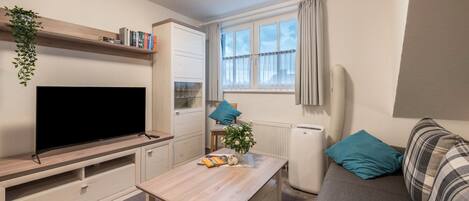 A modern living room with a flat-screen TV, a wooden coffee table, a sofa, a window with curtains, and a radiator.