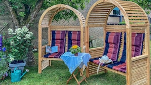 Una pérgola de madera con asientos acolchados y una mesa cubierta con un mantel de encaje.