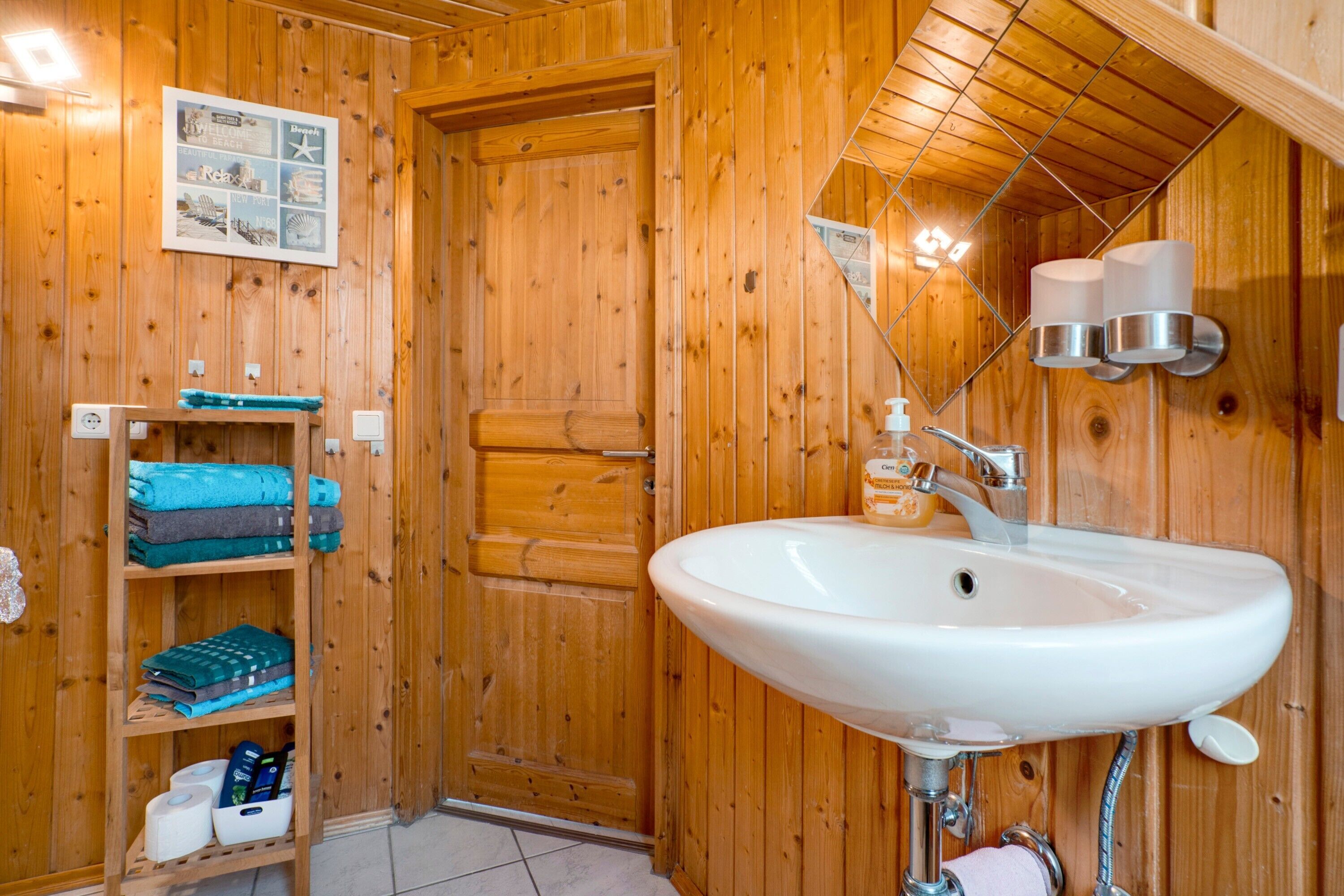 A wooden interior with a white sink, a shelf with towels, and a door.
