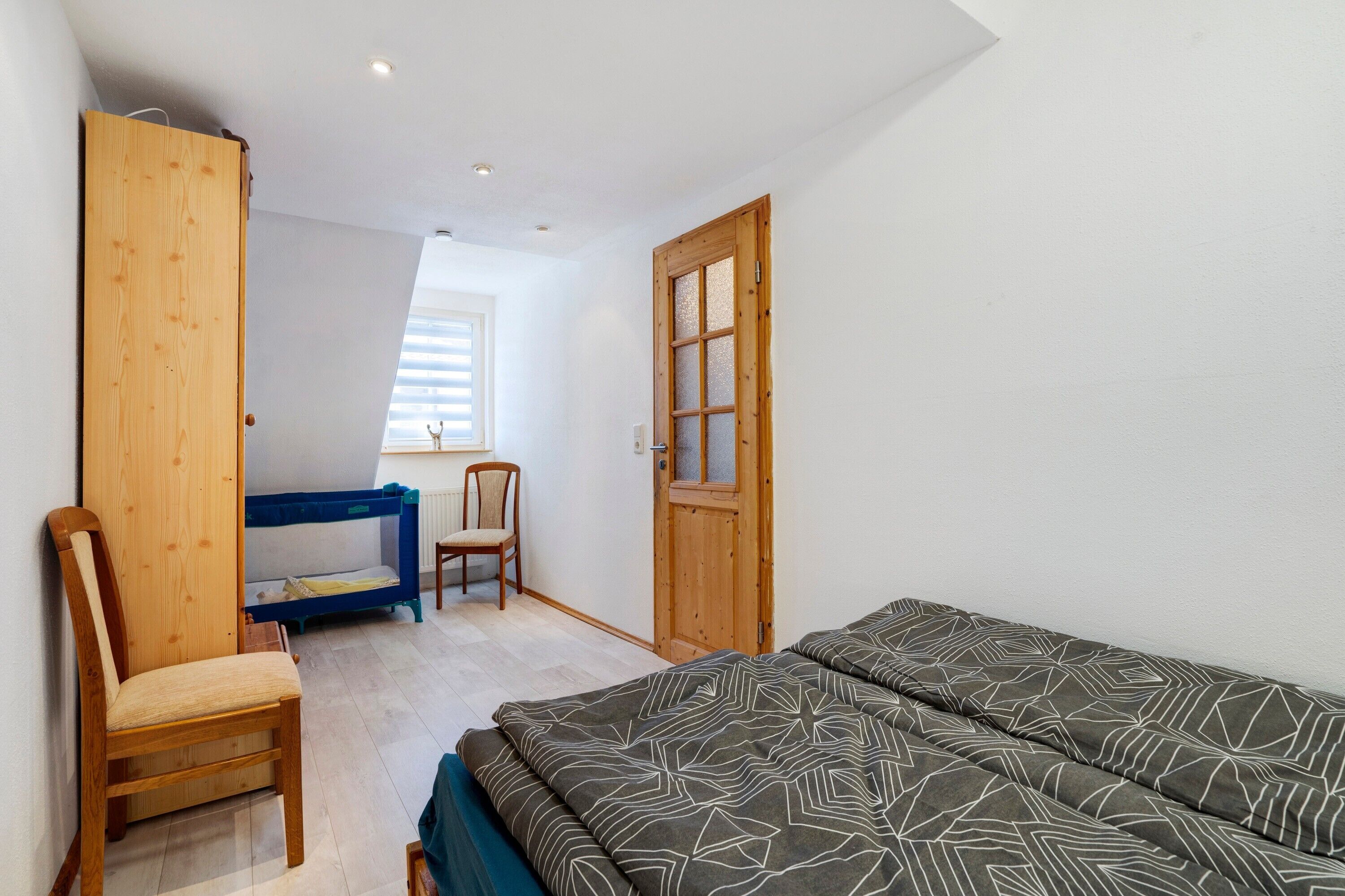 Een slaapkamer met een bed, een stoel, een stapelbed en een houten garderobe.
