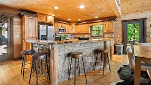 A wooden cabin with a stone island bar, wooden bar stools, and a dining area with a table and chairs.
