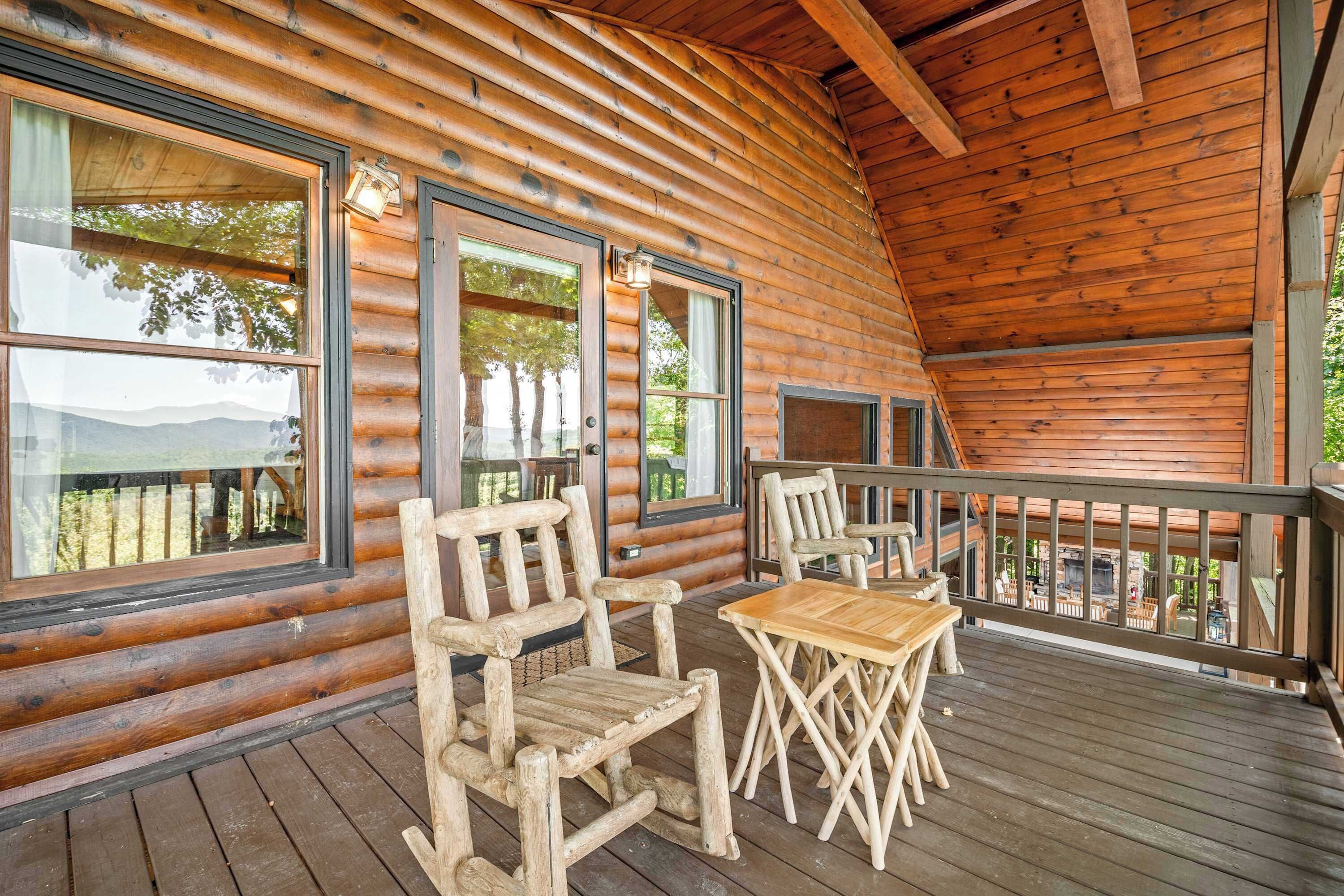 A log cabin with a wooden deck, large windows, and a dining area with chairs and a table.