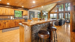 A spacious kitchen with wooden cabinets, a stone island, and a large window overlooking a scenic view.