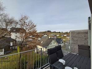 A balcony with a table and chairs, overlooking a residential area with houses and trees.