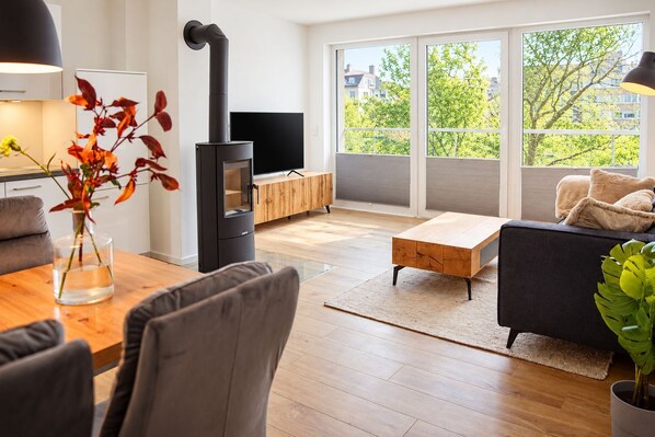 A modern living room with a black wood-burning stove, a wooden dining table, a sofa, and a TV.