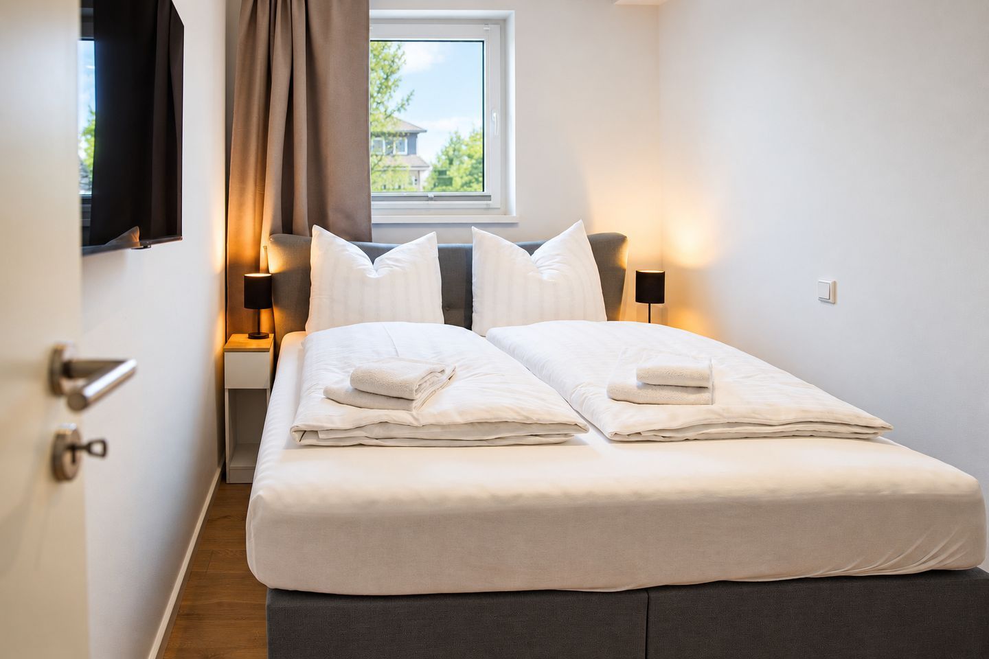 Une chambre d’hôtel avec un lit, deux tables de chevet, une fenêtre avec des rideaux et une vue sur la verdure.