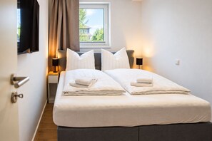 Ett hotellrum med en säng, två sängbord, ett fönster med gardiner och utsikt över grönområden utanför.
