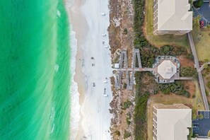 An aerial view of a coastal area with a beach, a pedestrian bridge, and buildings.