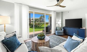 A modern living room with a large TV, comfortable seating, a coffee table, and a view of a landscaped garden.