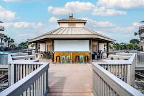 A beachside outdoor cinema with a large screen, wooden deck, and seating area.