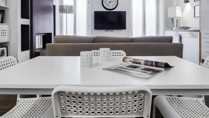 A modern living room with a white sofa, a flat-screen TV, a clock, and a dining table with chairs. - Italianway Comfort - Torino 57 A (Milan)