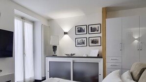 A hotel room with a bed, a desk with a lamp, a TV, and a wall with framed pictures. - Italianway Comfort - Torino 57 A (Milan)