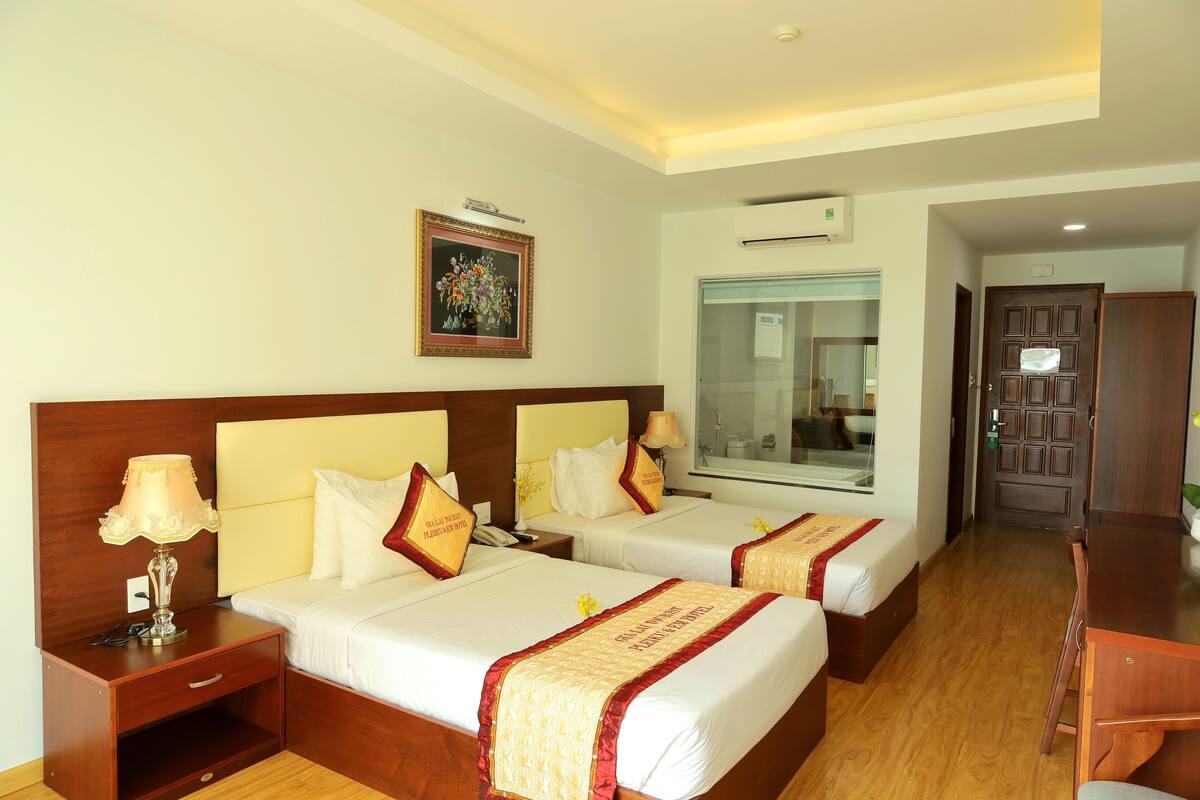 A hotel room with two beds, a desk, a mirror, and a window.