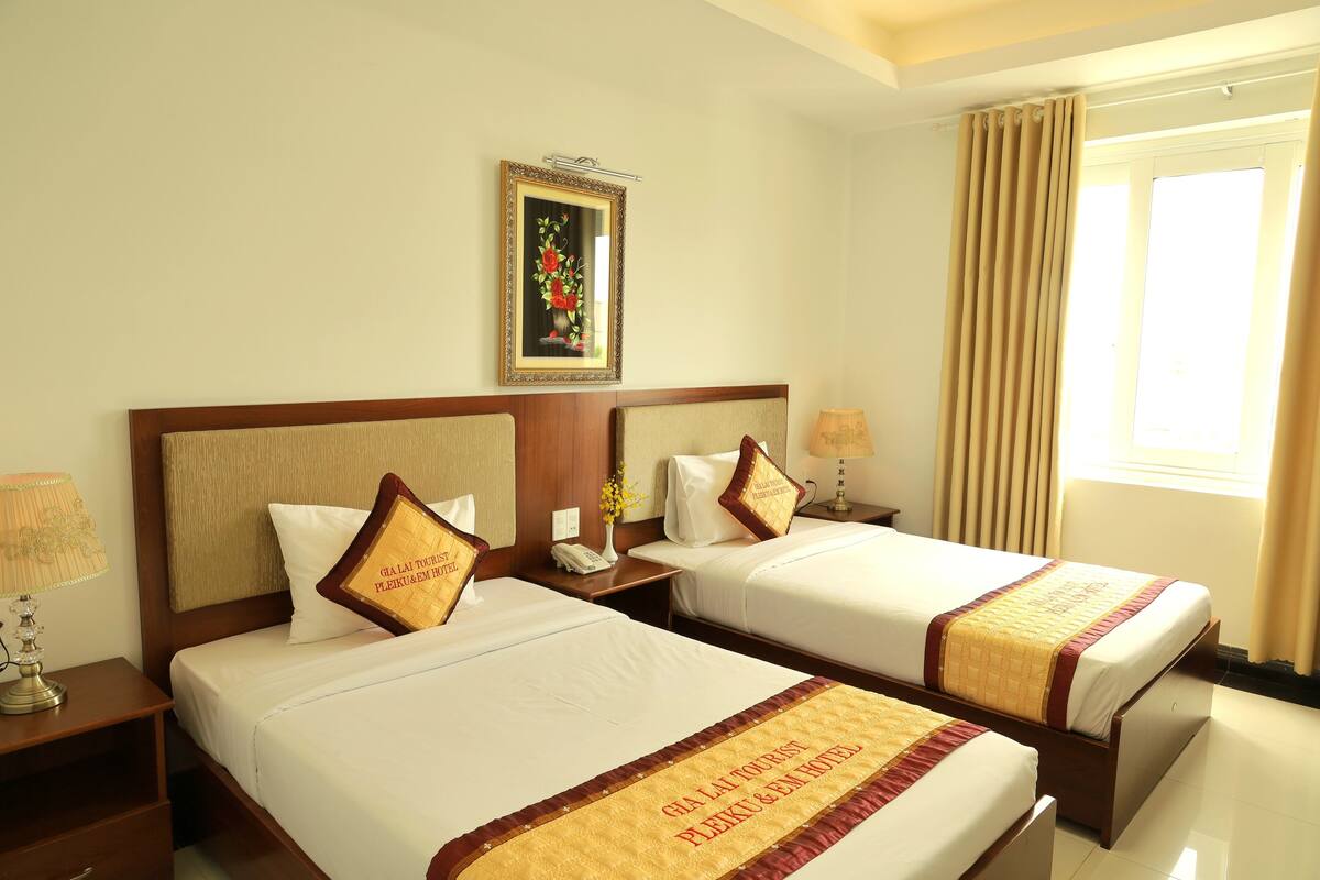 A hotel room with two beds, a nightstand with a lamp, a framed picture on the wall, and a window with curtains.