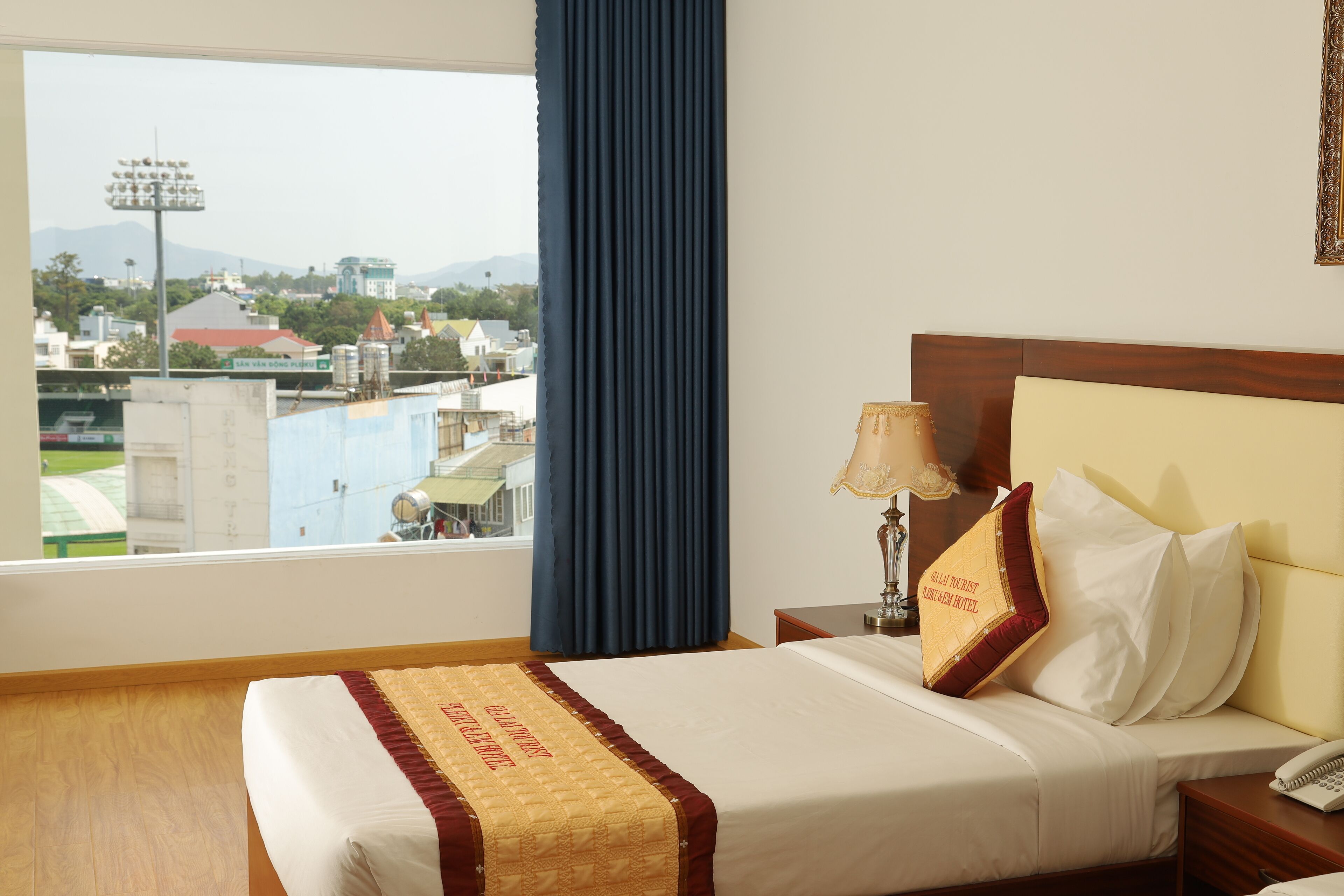 Une chambre d’hôtel avec un grand lit, une table de chevet, une lampe et une vue sur le paysage urbain par la fenêtre.