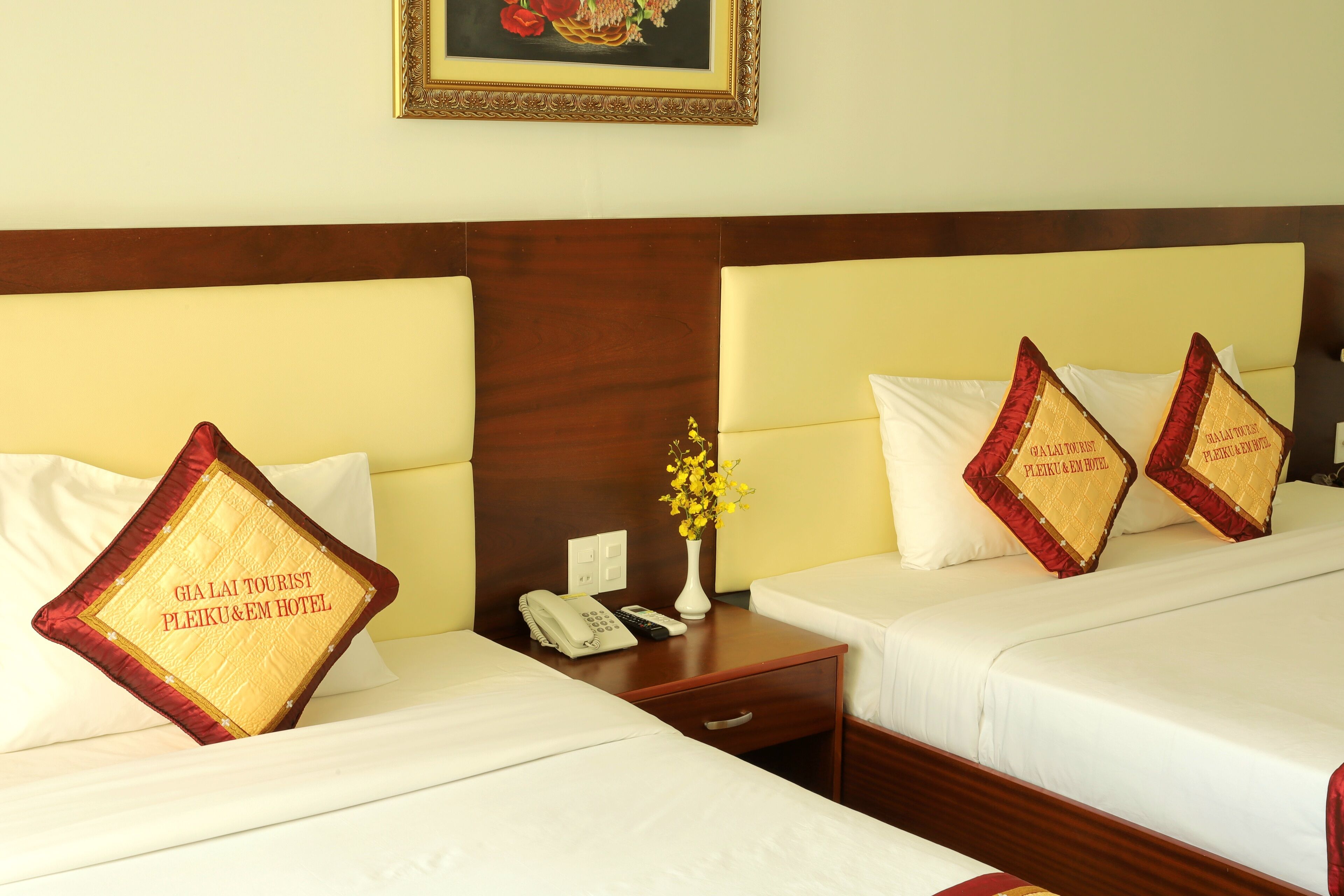 Two twin beds with matching headboards, a bedside table with a phone and a vase of flowers, and decorative pillows with text.