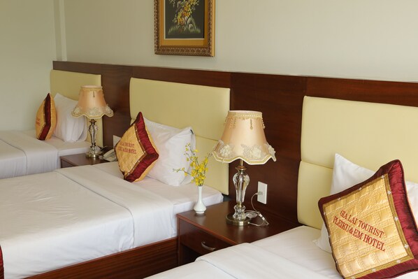 A hotel room with two beds, each with white linens and decorative pillows. There are two bedside tables with lamps and a vase with flowers.