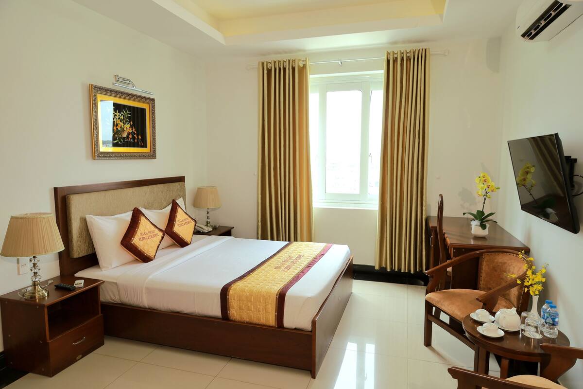 A hotel room with a bed, bedside tables, a desk with a chair, a TV, and a window with curtains.