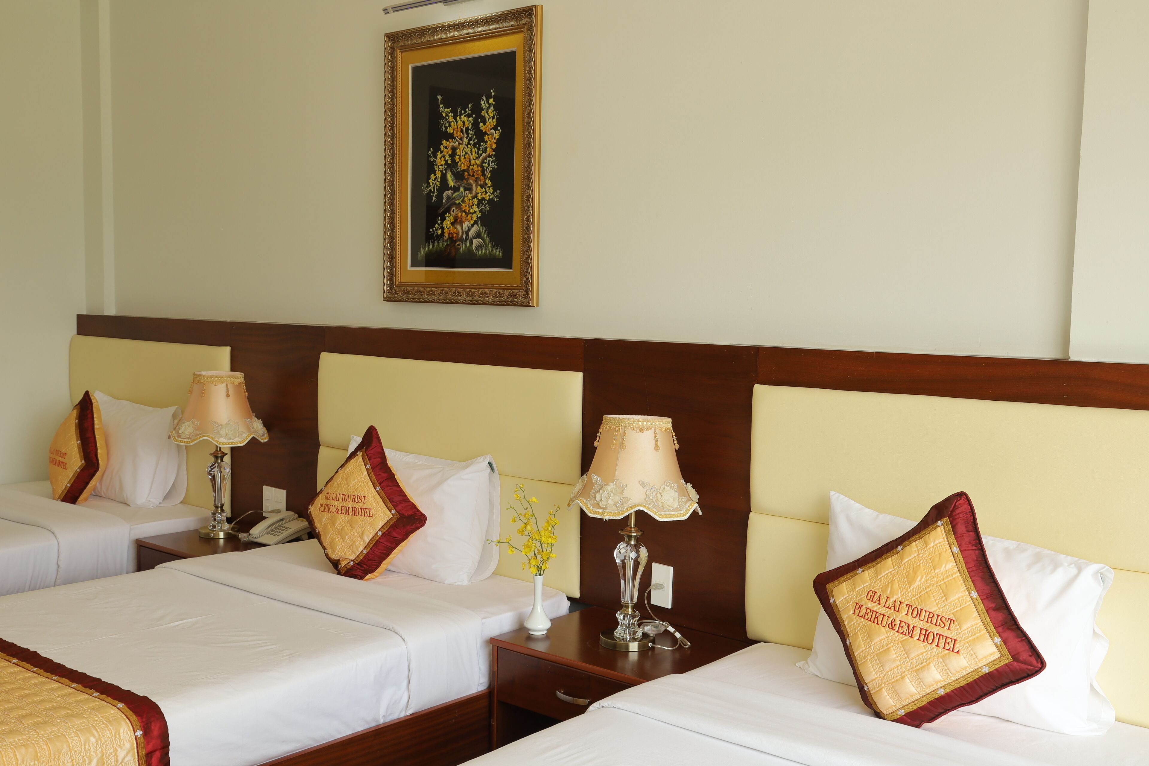 A hotel room with two beds, each with a lamp and a decorative pillow. There is a painting on the wall above the beds.