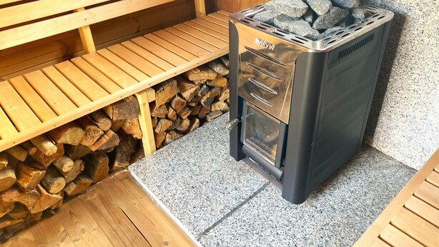 Una estufa de leña con chimenea metálica, un banco y una pila de leña.