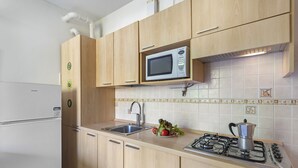 Een keuken met houten kastjes, een RVS spoelbak, een magnetron en een gasfornuis.