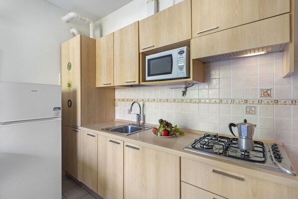 Una cocina con armarios de madera, un lavamanos de acero inoxidable, un microondas y una estufa a gas.