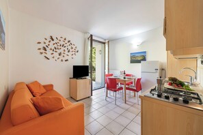 A compact living space with a sofa, a TV, a dining area with red chairs, and a kitchen with a stove.