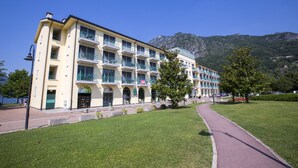 Een hotel met meerdere verdiepingen, balkons, een geplaveid pad en een berg op de achtergrond.