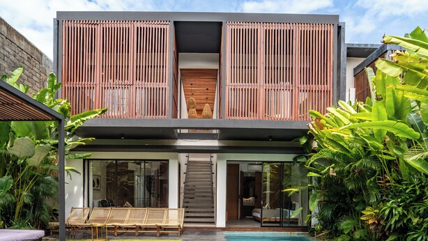 A modern two-story house with a swimming pool, a wooden deck, and lush greenery. - Red Sunset Villa by Betterplace (Canggu)
