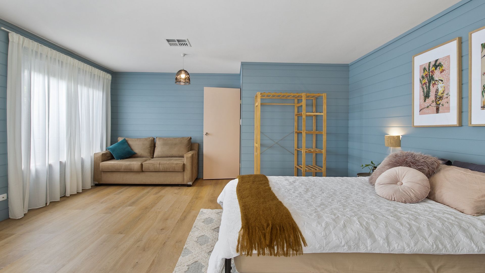 A bedroom with a bed, a sofa, a wooden ladder, a door, and a window with curtains.