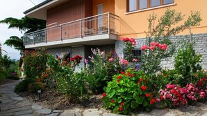 Een tweelaags huis met een balkon, omgeven door een tuin met diverse bloeiende planten.