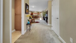 A hallway with a carpeted floor, a dining area with a table and chairs, and a kitchen in the background. - Perfect Retreat! 30 Nights Min! Raised Hot Tub With Views! (San Tan Valley)