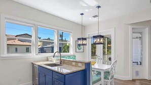 Een keuken met een blauw kookeiland, witte muren en een eethoek met een witte tafel en stoelen.