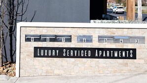 Un immeuble sur lequel on peut lire l’inscription « The Elm », et en dessous, une autre inscription indiquant « Appartements de luxe avec services ».