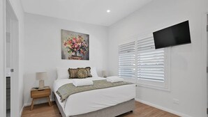 Une chambre à coucher avec un lit, un tableau, une télévision et une fenêtre avec des stores.