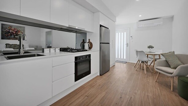 Une cuisine moderne avec des meubles blancs, un four encastré, un réfrigérateur en acier inoxydable et un coin repas comprenant une table et des chaises.