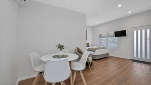 Une pièce moderne et bien éclairée, comprenant un coin repas, un canapé et un téléviseur fixé au mur.
