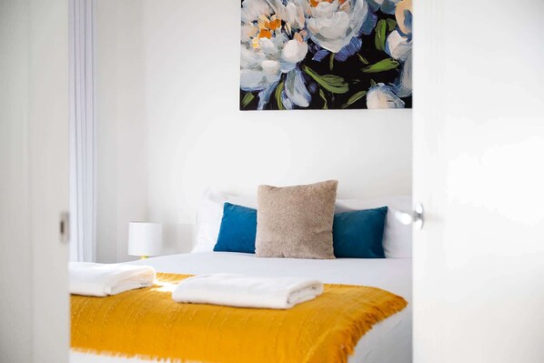 A hotel room with a bed, pillows, a blanket, and a painting on the wall.
