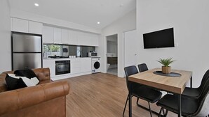 A modern kitchen with white cabinets, a stainless steel refrigerator, and a dining area with a wooden table and black chairs. - The Elm Apartments - The Cowhide Room (Orange)