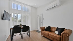 A modern living room with a brown leather sofa, black chairs, a dining table, and a TV mounted on the wall. - The Elm Apartments - The Cowhide Room (Orange)