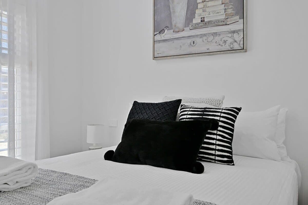 A neatly made bed with a black and white striped pillow, a black pillow, and a white pillow.
