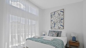 Een slaapkamer met een groot bed, witte gordijnen, een wandkunstwerk en nachtkastjes met lampen.