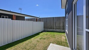 A modern house with a fenced backyard, a visible satellite dish, and a large window on the right side. - The Elm Apartments - The Green Room (Orange)