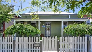 A two-story house with a white picket fence, a number 18 sign, and lush greenery. - Autumn Leaf Cottage - Close to CBD, Heritage Charm (Orange)