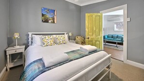 A bedroom with a bed, nightstands, a ceiling fan, a door, and a view into another room. - Autumn Leaf Cottage - Close to CBD, Heritage Charm (Orange)