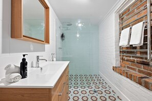 A bathroom with a white sink, wooden cabinets, a glass shower enclosure, and a patterned floor. - Autumn Leaf Cottage - Close to CBD, Heritage Charm (Orange)