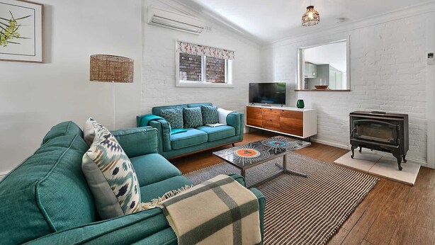 A modern living room with a teal sofa, a wooden cabinet, a television, a fireplace, and a large mirror. - Autumn Leaf Cottage - Close to CBD, Heritage Charm (Orange)